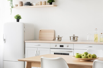 Cozy kitchen design with utensils. White furniture, stove with kettles, wooden cutting board, small refrigerator