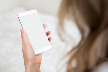 A woman's hand holds a smartphone with a white screen on a white room background