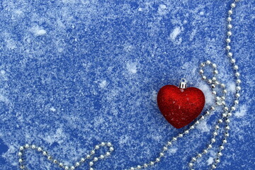 On a blue background lies snow with a garland and a Christmas tree toy heart.