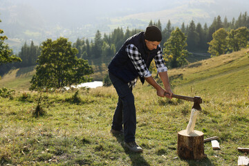 Handsome man with axe cutting firewood on hill - Powered by Adobe