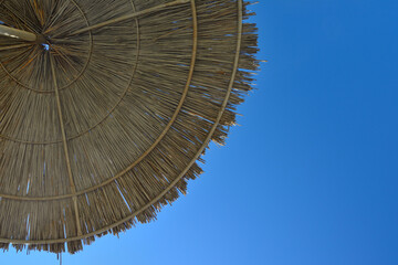 Beach umbrella, awning, canopy made of straw and reeds against a clear blue sky, on the beach on a sunny day