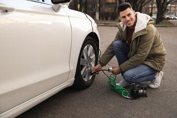 Handsome man inflating car tire with air compressor on street