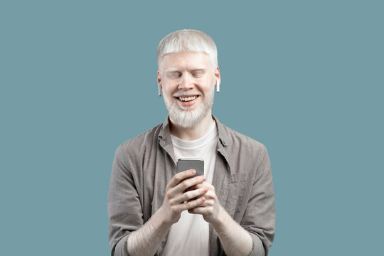 People and technology concept. Excited albino man using smartphone, standing isolated over blue studio background - Powered by Adobe