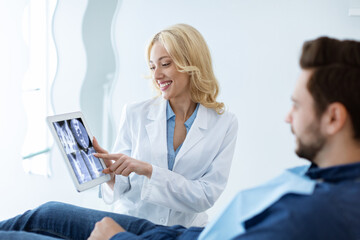 Obraz na płótnie Canvas Female dentist showing man patient treatment goal, using tablet