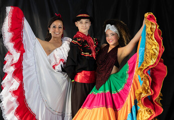 Three Colombian dancers dressed in traditional folklore costumes in studio with black backdrop