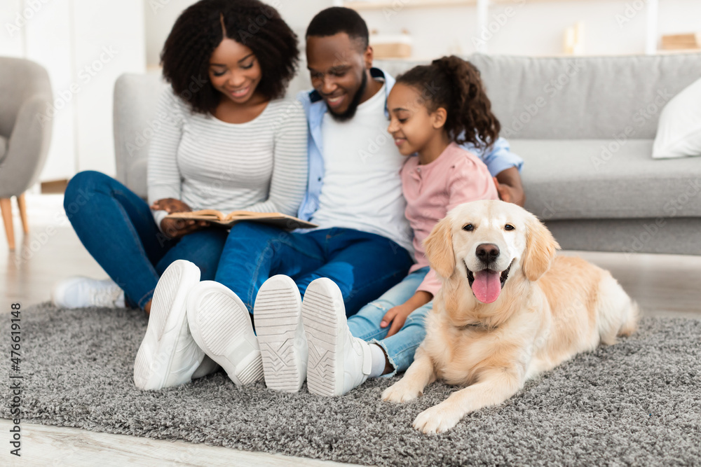 Wall mural young black family reading book with dog at home