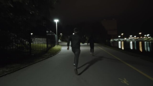 Handheld rear view shot of one unrecognizable man is chasing another faceless man in the city street at night. Pursuit of a thief at night