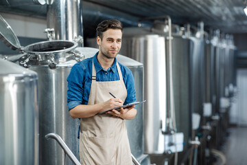 Serious man using brewing equipment at factory. Control of plant, collect data