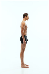 Profile view of young handsome shirtless sportive man wearing black boxer-briefs standing isolated on white studio background.