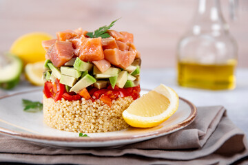 Salmon tartare with tomatoes, avocado and quinoa on a plate and light gray table
