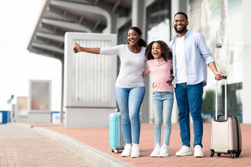 Happy black family traveling with kid, catching taxi at airport