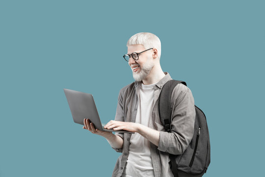 Cool guy with unusual appearance using laptop for online work or studies, wearing backpack over turquoise background