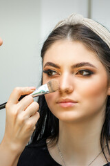 Fototapeta premium Closeup portrait of a woman applying dry cosmetic tonal foundation on the face using a makeup brush. Makeup detail
