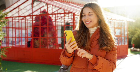 Panoramic banner of beautiful smiling woman in puffer jacket holding smartphone on christmas time