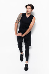 Full length of tattooed man in sportswear standing on grey background