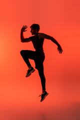 Fototapeta na wymiar Side view of sportsman jumping on red background