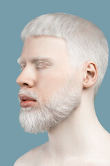 Fototapeta premium Skin abnormality concept. Portrait of young albino man with pale skin, white hair and beard against turquoise background
