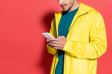Cropped view of sportsman in yellow sports jacket using mobile phone on red background
