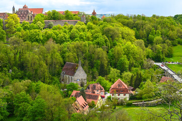 A historic church and old houses in a valley surrounded by forest near the city of Rothenburg ob der Tauber, Germany.