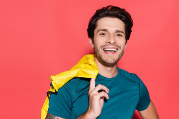 Smiling sportsman holding yellow sports jacket and looking at camera on red background
