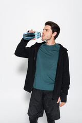 Sportsman in sports jacket drinking water on grey background