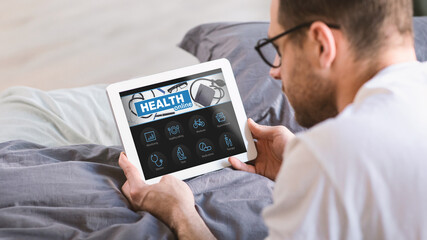 Man Using Digital Tablet While Lying In Bed