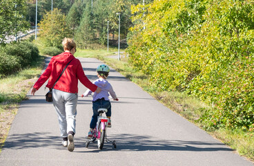 Cycling ride. Young caucasian woman teaches a child to ride a bike. A child in a bicycle helmet.