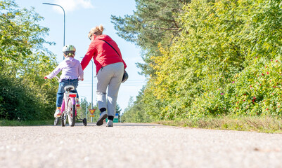 A girl, blonde, teaches a child to ride a bike. Walk on the bike path on a summer day