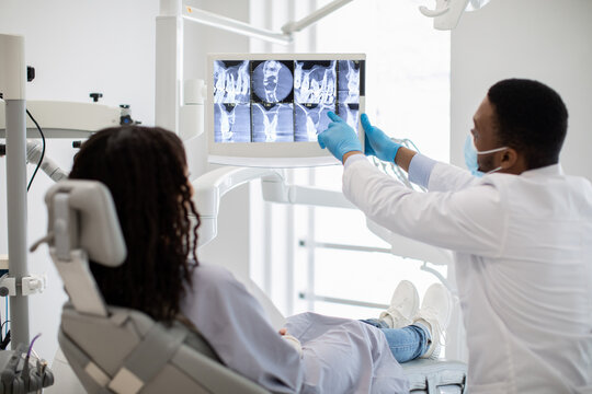 Black Stomatologist Showing Treatment Result At Teeth Xray Picture To Female Patient