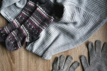 Fototapeta na wymiar Gray sweater, warm gloves and socks on wooden background. Top view.