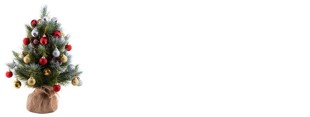 Christmas pine tree in a pot wrapped in cloth. Decorated with colorful balls, cones, and red berries. Tips of pine branches covered with snow. Isolated on white background. Copy space. Banner size