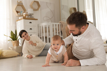 Happy parents helping their baby to crawl on floor at home