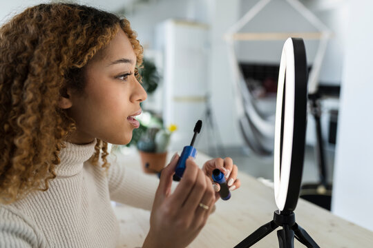 Black woman applying mascara in front of ring lamp