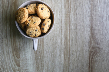 Ceramic bowl filled with chocolate chip cookies on wooden table. Flat lay.