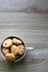 Ceramic bowl filled with chocolate chip cookies on wooden table. Flat lay.