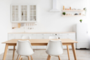 Blurred kitchen interior in scandinavian style with wooden dining table and chairs on foreground
