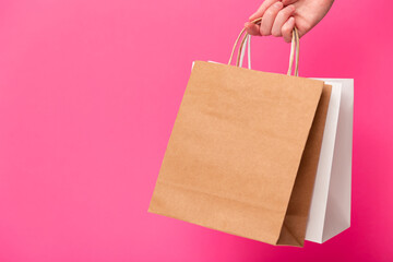 Female hand holding two shopping bags isolated on pink background. White and brown craft blank...