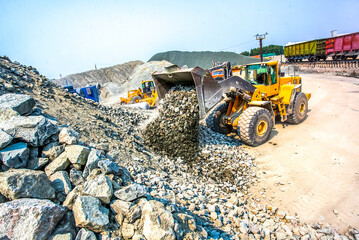 Yellow digger bulldozer working in quarry near train
