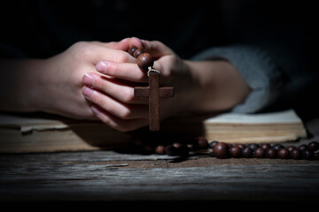 Young beautiful girl praying to God with wooden rosary.