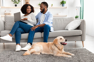Black couple at home using laptop sitting with dog