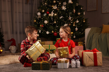 Cute little children with gift boxes near Christmas tree at home