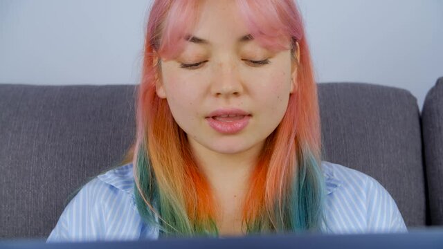 Confused freelancer girl with dyed hair communicating with clients online while working from home on lockdown. Individual young woman with colored hair works free lance on laptop computer