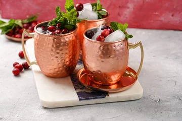 Schilderijen op glas Traditional american alcoholic beverage moscow mule in copper mugs with cranberry and mint on white marble board - non-alcoholic cocktail version © Romana
