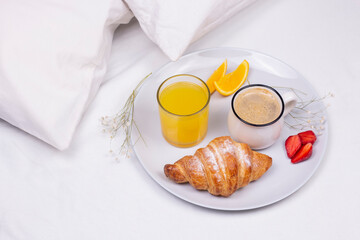 Romantic morning breakfast in bed. Orange juice, croissant and strawberry on the plate.