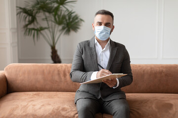 Portrait of professional male therapist in mask sitting on sofa