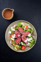 Modern style traditional fried dry aged bison beef rump steak slices with vegetable, lettuce and raspberry mustard dressing served as top view on a Nordic design plate