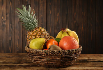 Fresh ripe fruits in wicker bowl on wooden table