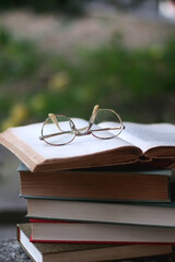 Stack of hardcover books and reading glasses in a garden. Selective focus.