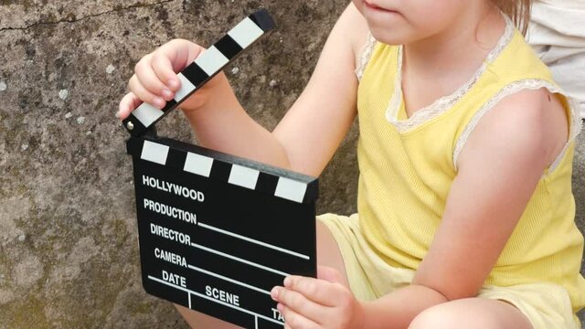 Elementary school age girl, child playing with a classic empty blank film movie clapperboard, dumb slate, outdoors hands closeup, one person, face obscured. Young director, movie producer concept
