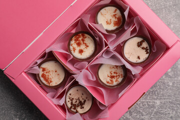 Delicious chocolate candies in pink box on light grey table, top view. Production line